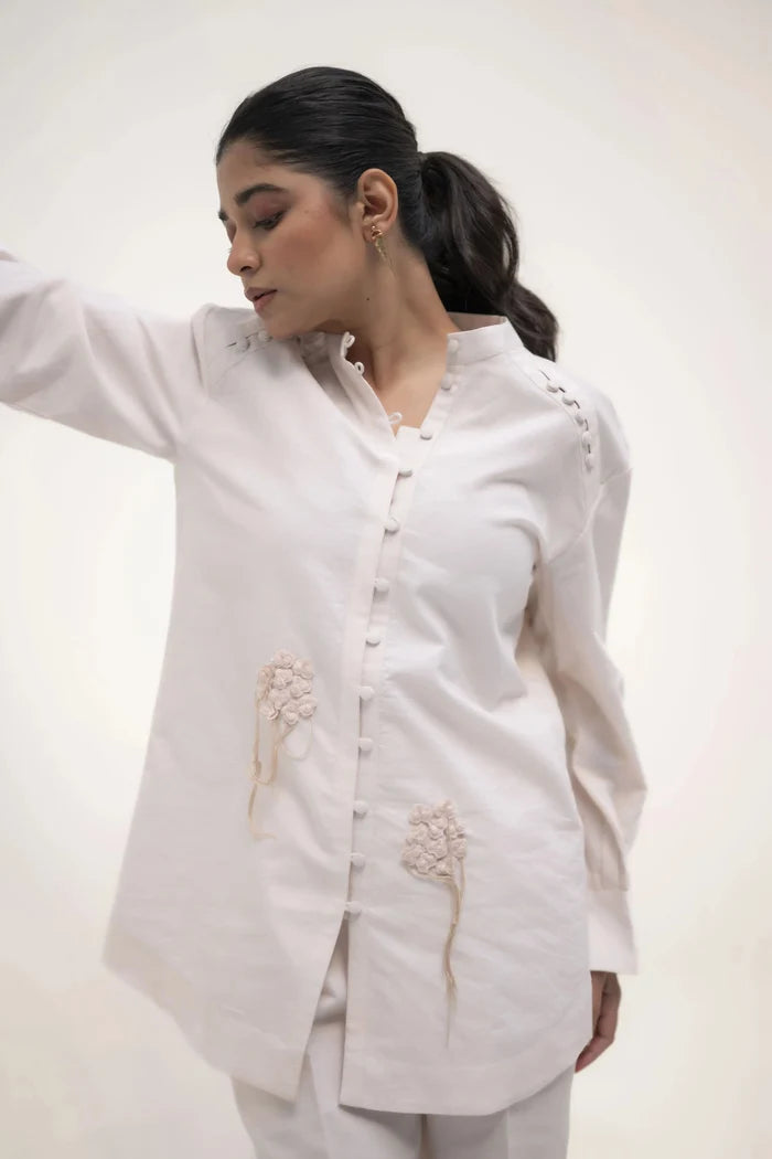 The model in a white shirt and trousers, with one arm raised, showcasing a relaxed and elegant stance.