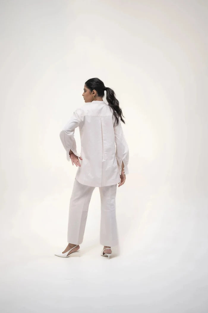 The model in a white shirt and trousers, striking a confident pose with one hand resting on her hip, facing the camera.