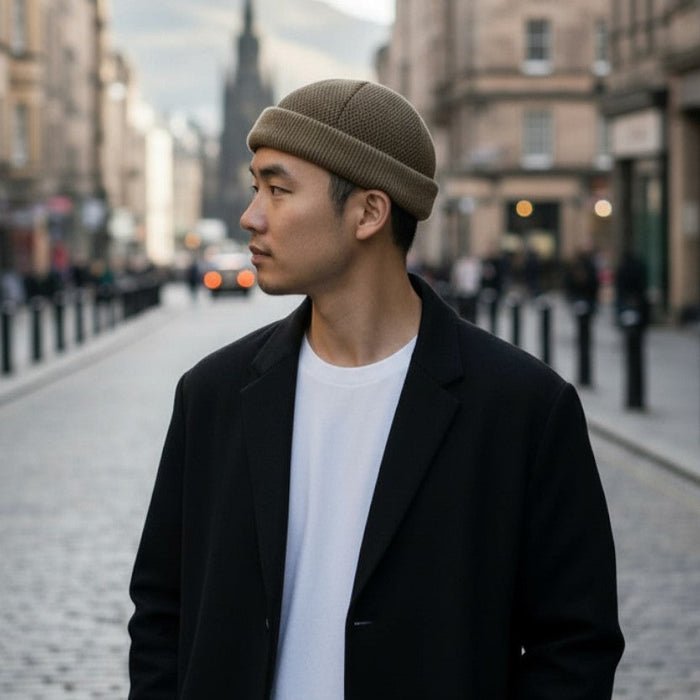 Man wearing a brown beanie and black coat standing on a city street.