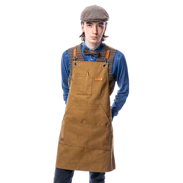 A person wearing a brown canvas utility apron with multiple pockets and adjustable straps, standing against a white background.