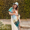 A woman wearing a sky blue felt fedora hat and a color block blanket scarf with blue and brown hues.